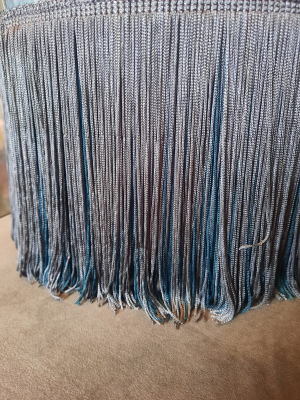 a close up image of grey and teal fringe detail on a footstool